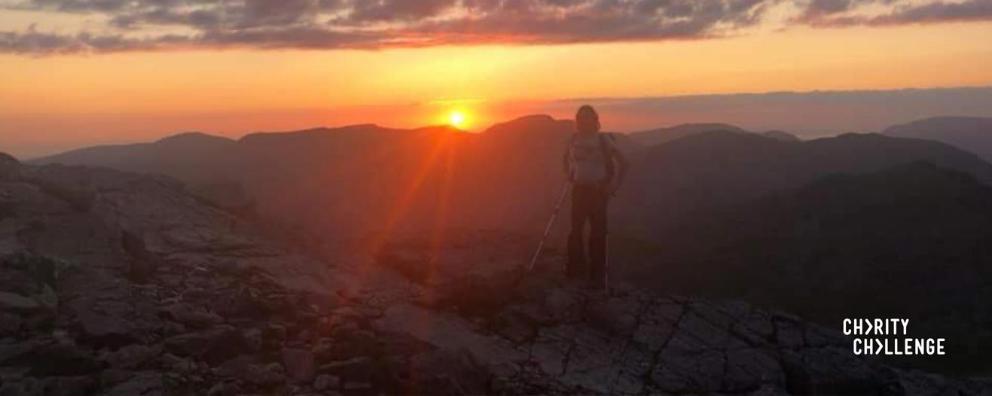 A person standing at the Ben Nevis summit as the sun rises.