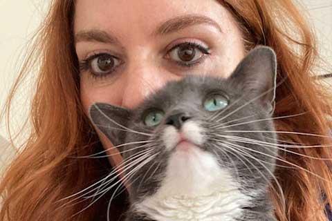 A head-shot of a woman holding a cat and the cat's face covers most of the woman's face.